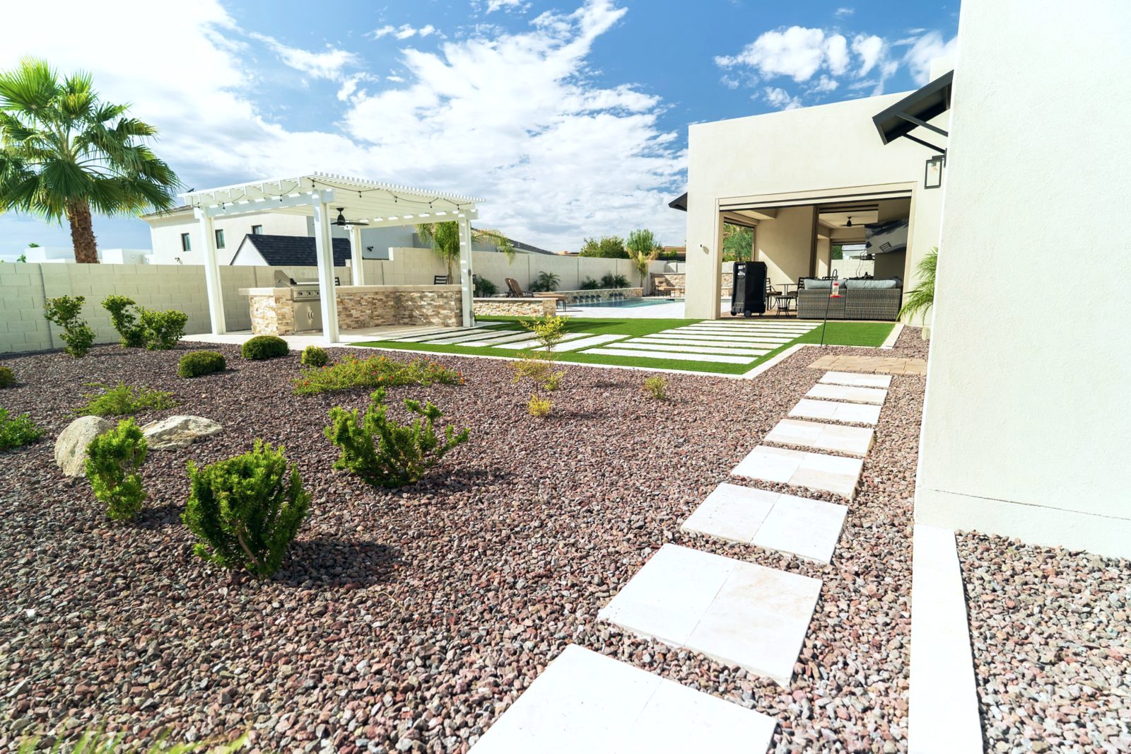 Desert backyard with pergola kitchen, turf strips and travertine path